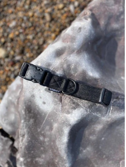 Black coloured dog collar made from recycled Ocean Plastics, lying on a rock on a beach